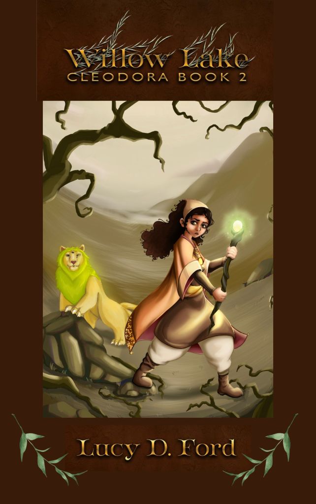 A young girl in orange robes advances from a dusty beige landscape. She has curly black hair and holds a glowing staff. Beside her is a yellow bobcat with a green mane. The image is framed in dark brown with a metallic gold headline. Text reads "Willow Lake, Cleodora Book 2, by Lucy D. Ford"